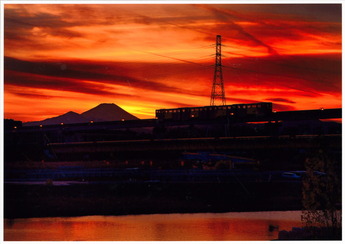 夕焼けの富士山をバックに立日橋を走るモノレールの写真