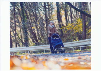 紅葉の中、女性が子供をベビーカーに乗せ散歩している写真